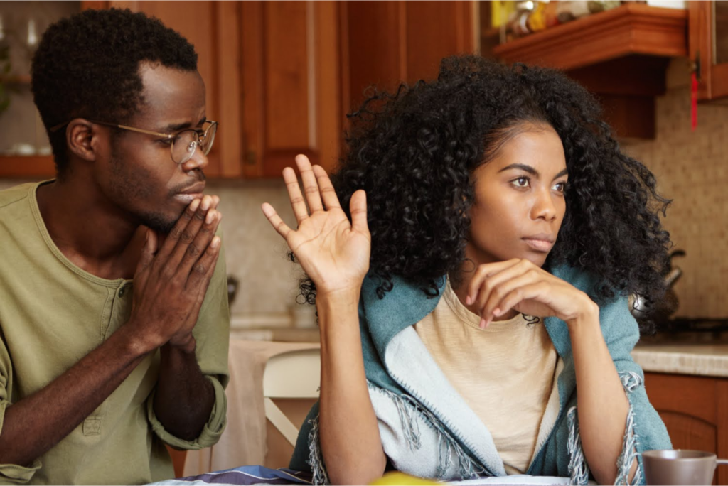 A man and a woman having a serious conversation, with the man appearing to plead and the woman looking away, raising her hand.