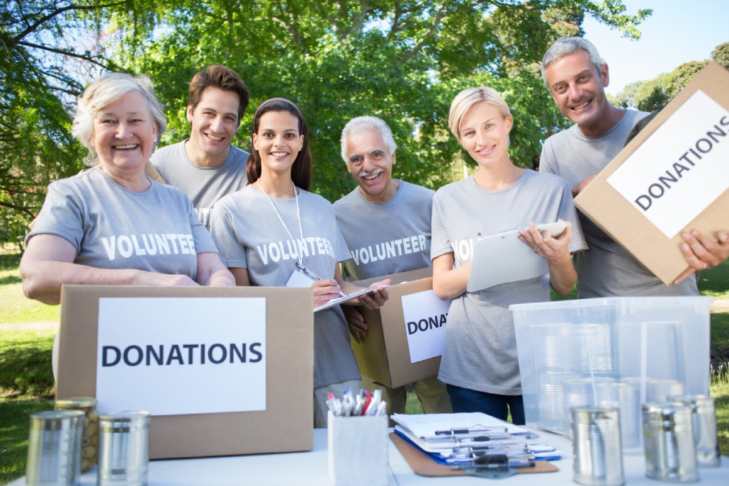 A group of smiling volunteers holding donation boxes, highlighting charitable donations as a strategy in estate planning.